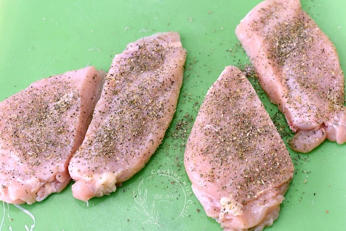 Four chicken breasts sprinkled with seasoning salt on a green plastic mat