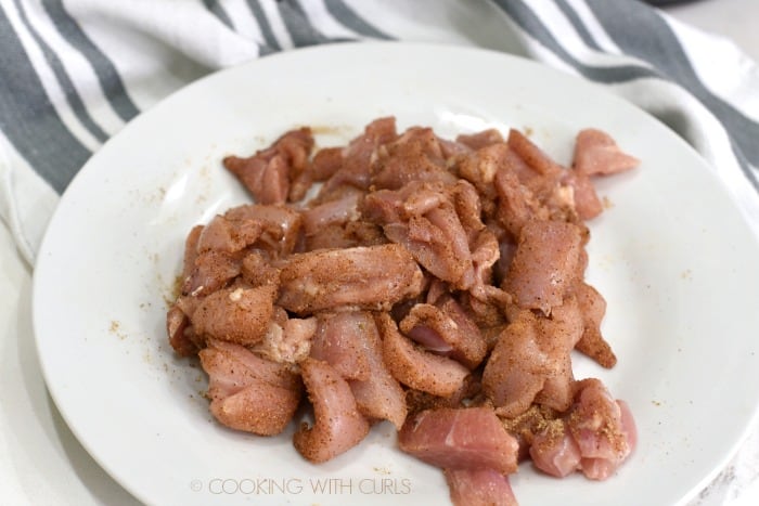Spice covered chicken pieces on a white plate, sitting on a gray and white striped towel