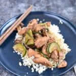 Instant Pot Chinese Garlic Chicken served over a bed of rice on a blue plate with wooden chopsticks in the upper left hand edge of the plate