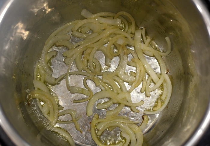 Thinly sliced onions cooking in oil inside a metal liner to a pressure cooker 