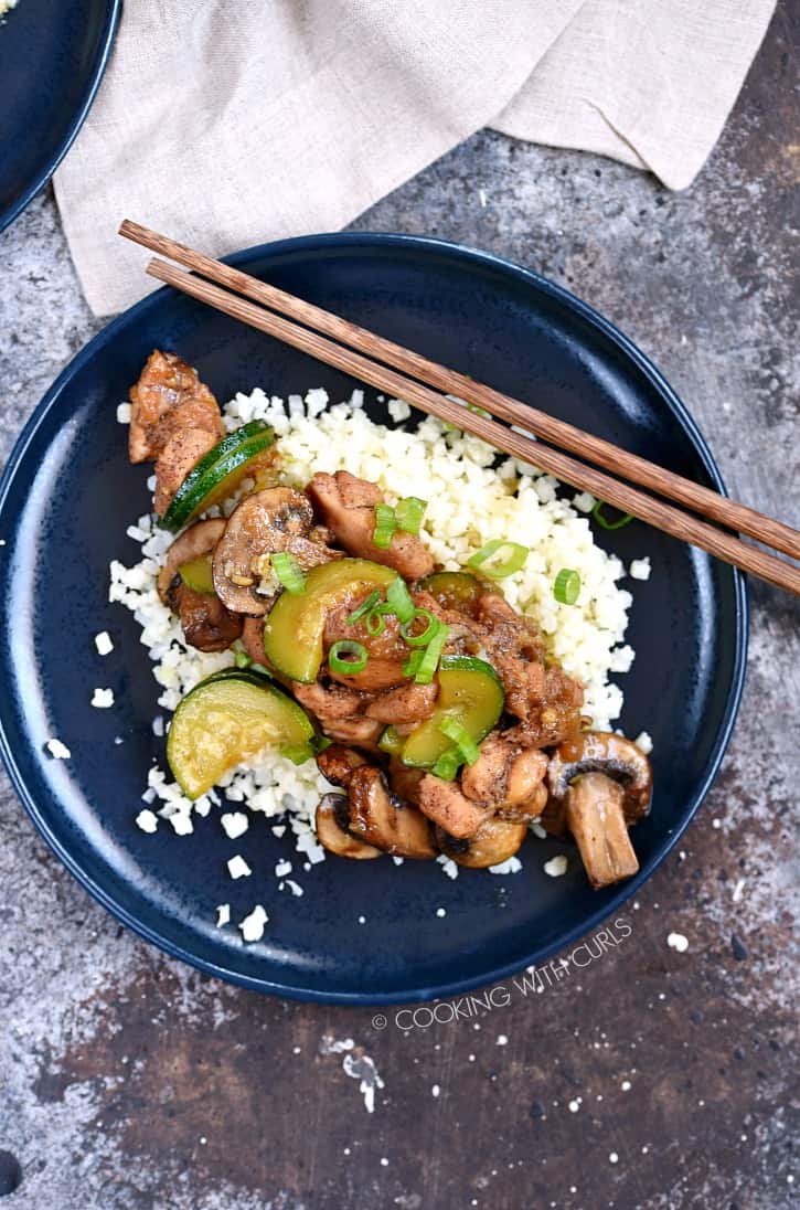 Instant Pot Chinese Garlic Chicken served over a bed of cauliflower rice, served on a blue plate with wooden chopsticks laying in the upper right hand corner of the plate