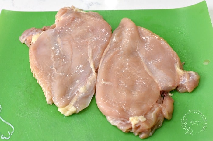 Two chicken breasts pounded flat on a green cutting mat 