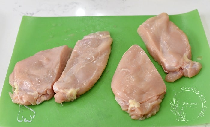 Two chicken breasts pounded flat then cut into 4 equal pieces sitting on a green cutting mat 