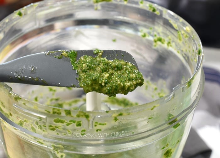 Chimichurri sauce scooped out of a food processor with a gray silicone spatula 