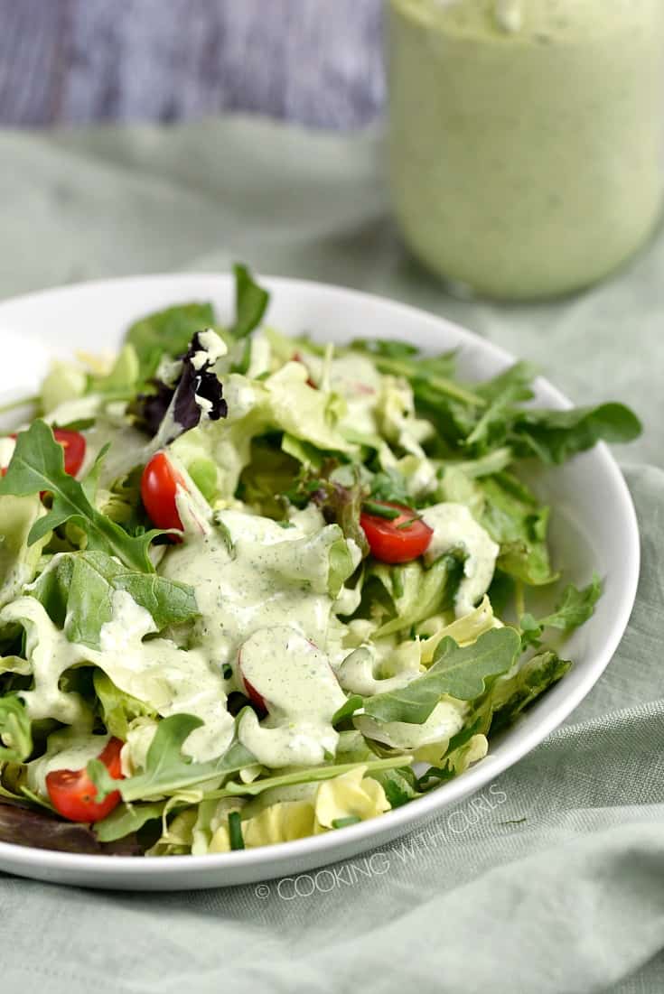 Salad greens topped with Green Goddess Dressing with a jar of dressing in the background.