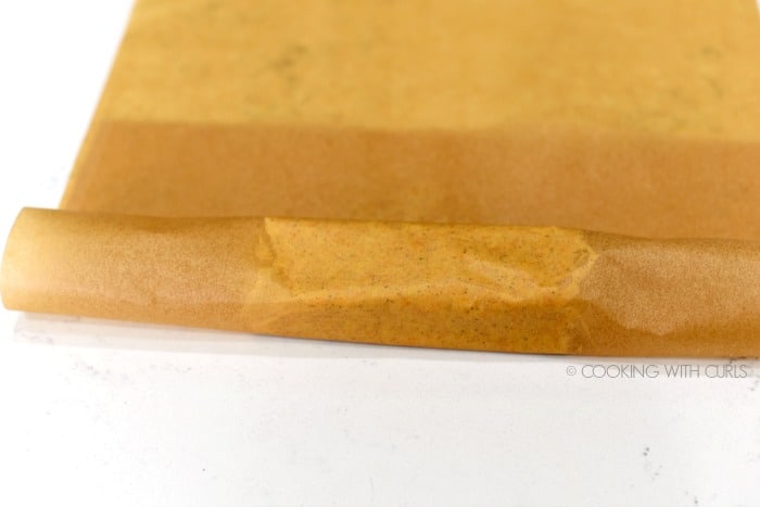 One side of the parchment paper rolled over the butter 