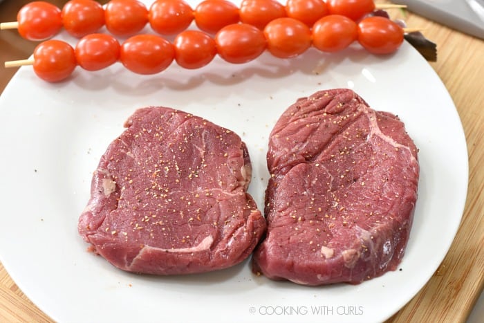 Seasoned sirloin steaks and skewered cherry tomatoes on a large white plate 