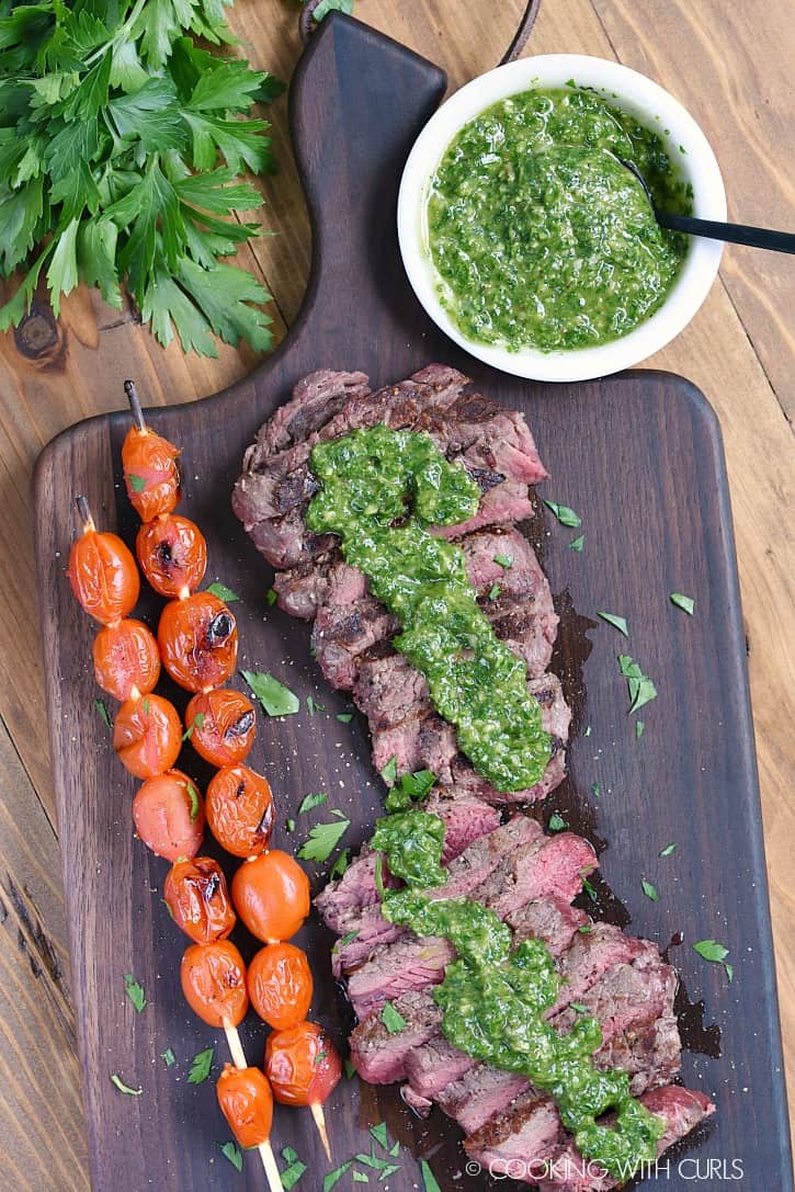 Two sliced sirloin steaks topped with chimichurri sauce with skewered tomatoes on the side.