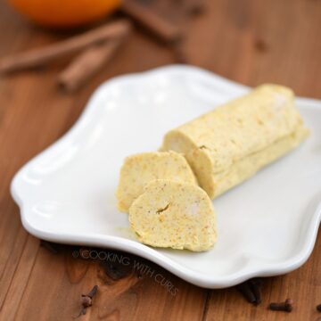 A chilled log of Asian 5-Spice Compound Butter sitting on a white plate with cinnamon sticks and an orange in the background