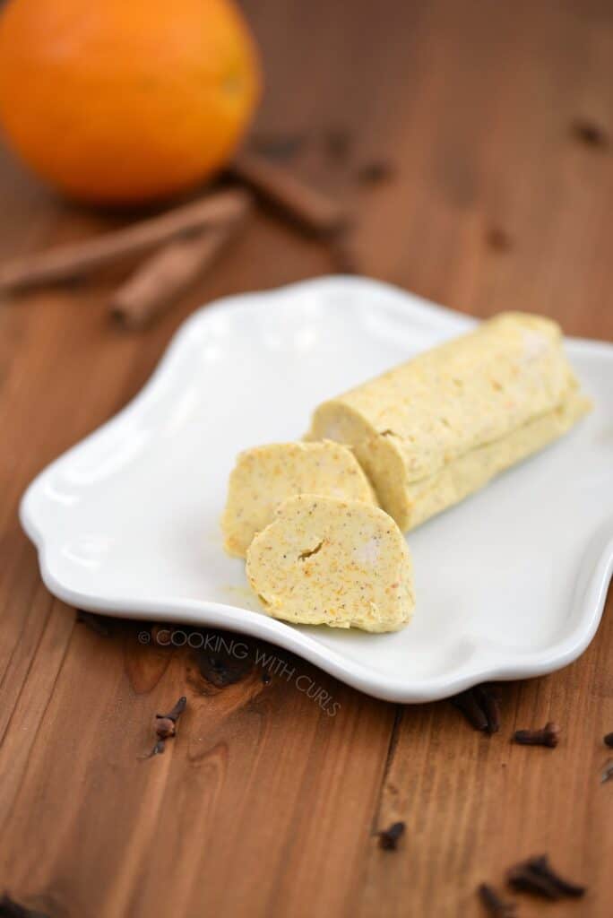 A chilled log of Asian 5-Spice Compound Butter sitting on a white plate with cinnamon sticks and an orange in the background