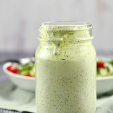 A jar of Green Goddess Dressing sitting in front of a bowl of salad greens.