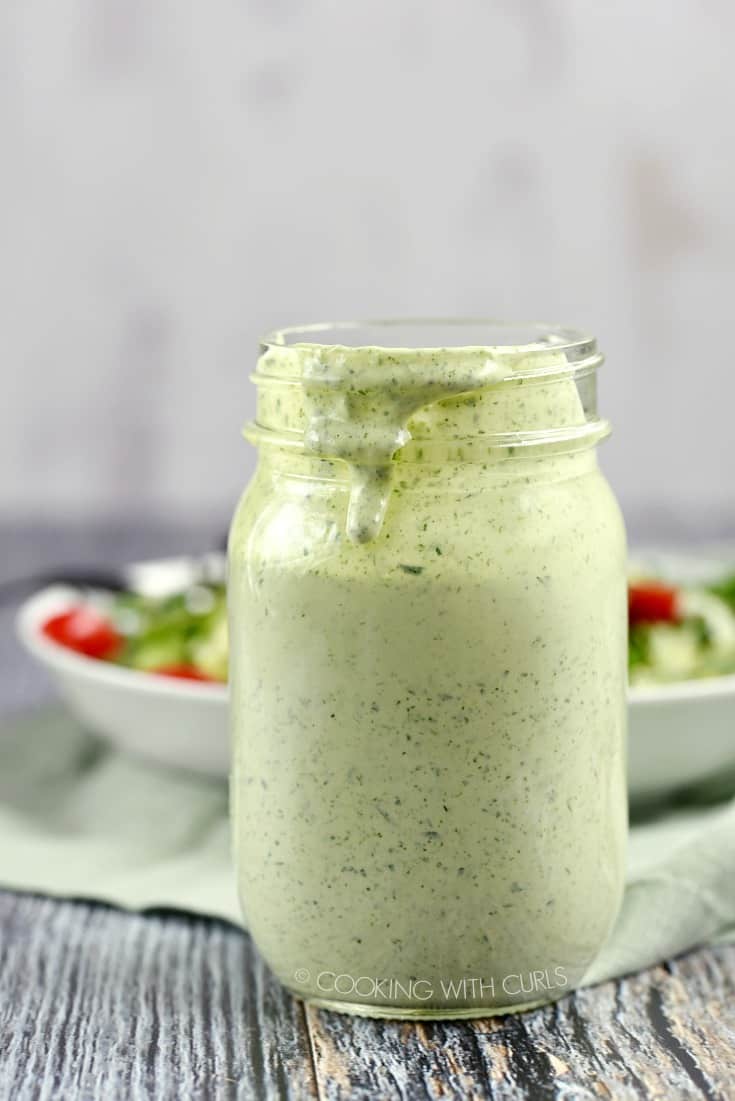 A jar of Green Goddess Dressing sitting in front of a bowl of salad greens.