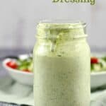 A jar filled with Green Goddess Dressing sitting in front of a bowl of salad greens.