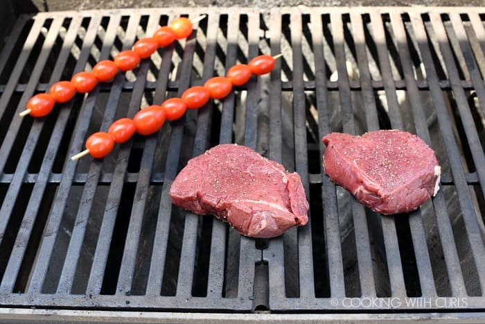 Two seasoned steaks and two skewers of cherry tomatoes on the grill 