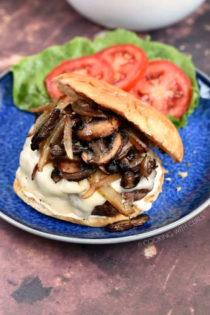 Mushroom Swiss Burgers on a blue plate with lettuce and tomato on the side