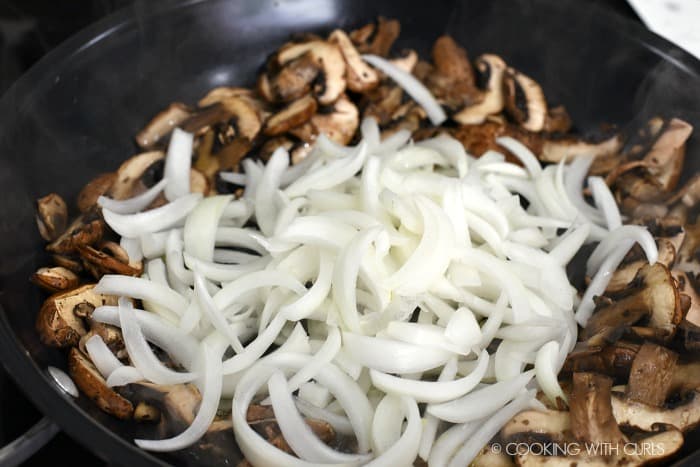 Add the sliced onions to the cooked down mushrooms in the skillet. 