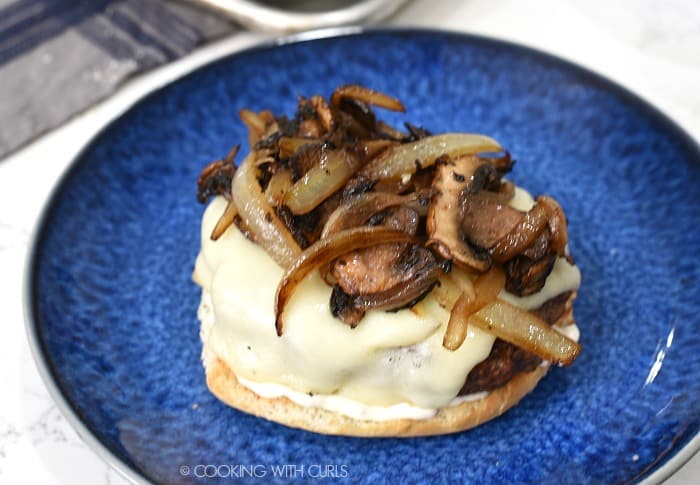 Caramelized mushrooms and onions on top of a cheese topped burger on a bottom bun. 