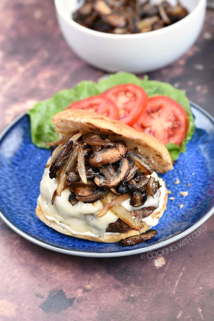 A cheese burger topped with caramelized mushrooms and onion with lettuce and tomato on the side