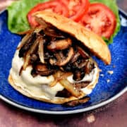 Mushroom Swiss Burgers on a blue plate with lettuce and tomato on the side.