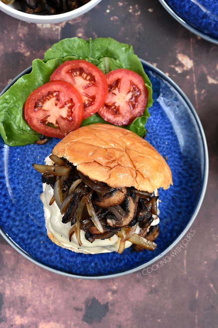 Overhead shot of a Mushroom Swiss Burger with lettuce and tomato on a blue plate.