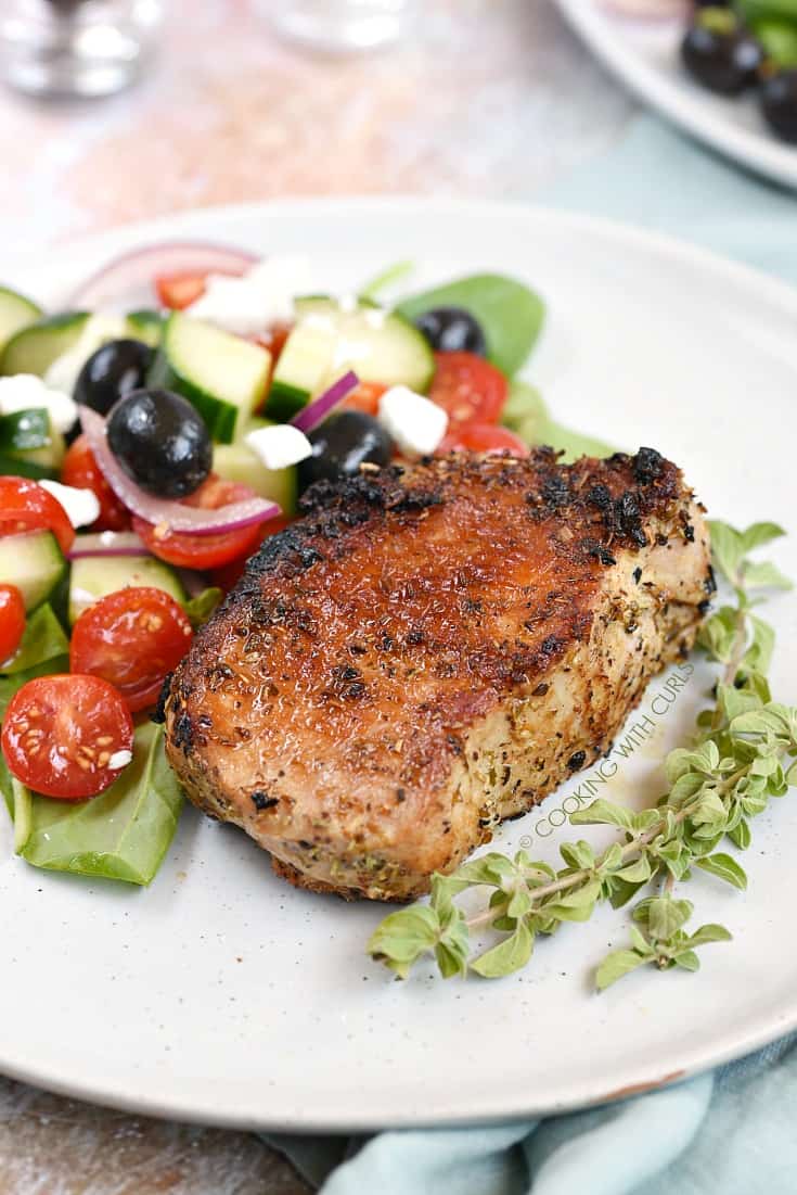 Boneless, Greek Pork Chops served with a Greek salad and sprigs of fresh oregano