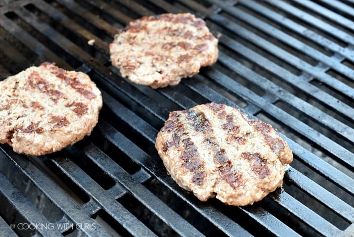 Three cooked burgers on the grill. 
