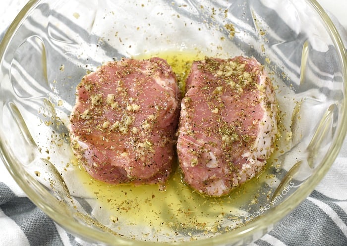 Two boneless pork chops in a large glass bowl with Greek marinade 