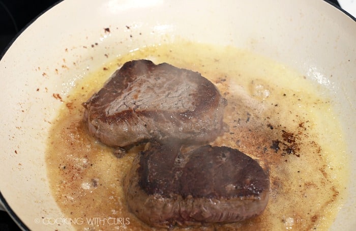 Two seared steaks in a skillet with hot oil and butter 
