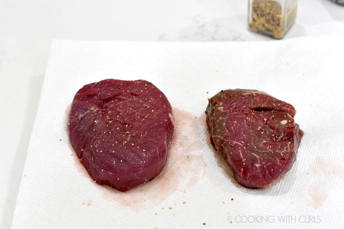 Two steaks seasoned with garlic pepper sitting on paper towels 