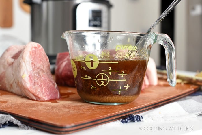 Cooking liquid in a measuring cup with pork pieces in the background 