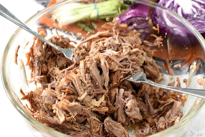Hawaiian Pork being shredded with two forks in a large glass bowl 