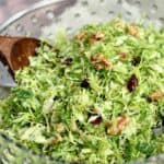A glass serving bowl filled with Shaved Brussels Sprouts Salad tossed with walnuts and cranberries