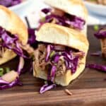 Hawaiian Pulled Pork sandwiches topped with pineapple slaw sitting on a dark wood serving board