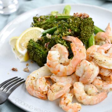 Shrimp, broccolini and lemon wedges on a large white plate