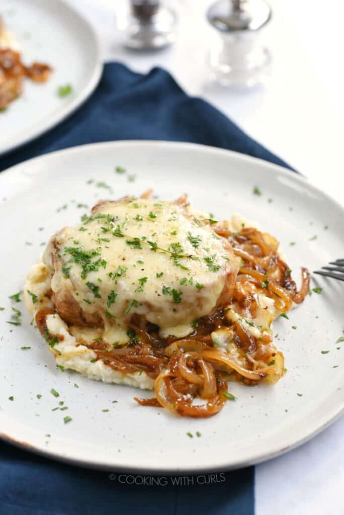 French Onion Pork Chop smothered in melted cheese and caramelized onions on a white plate