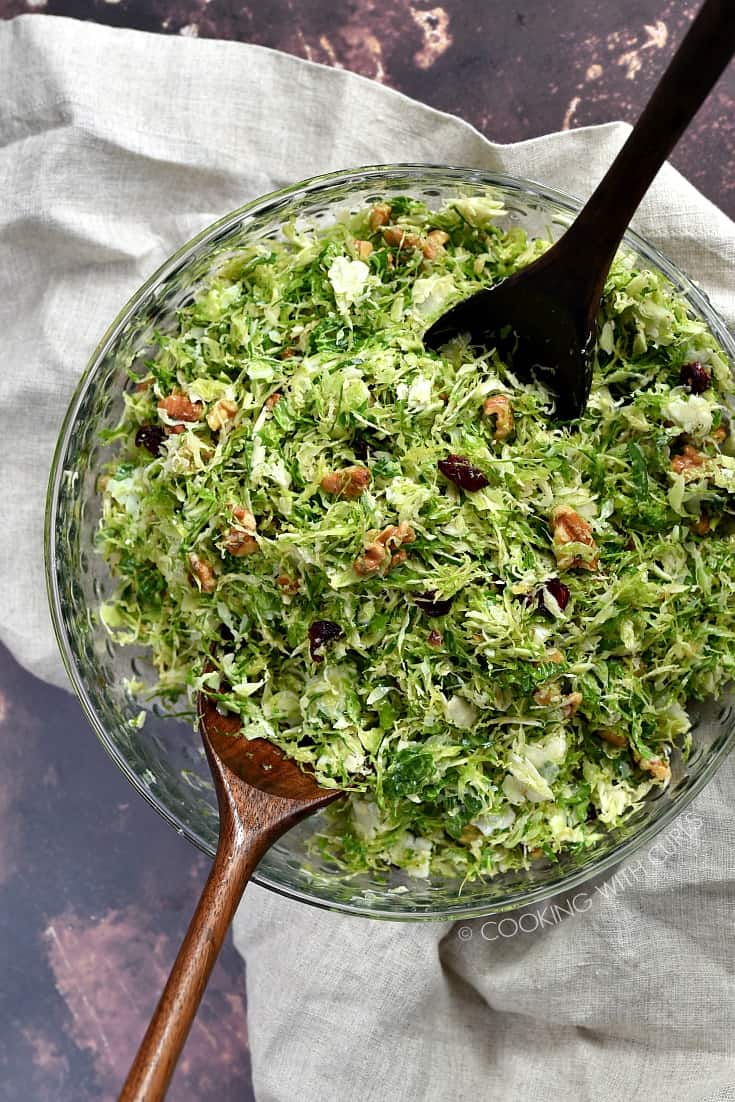 An overhead image of a Shaved Brussels Sprouts Salad tossed together in a clear glass serving bowl.