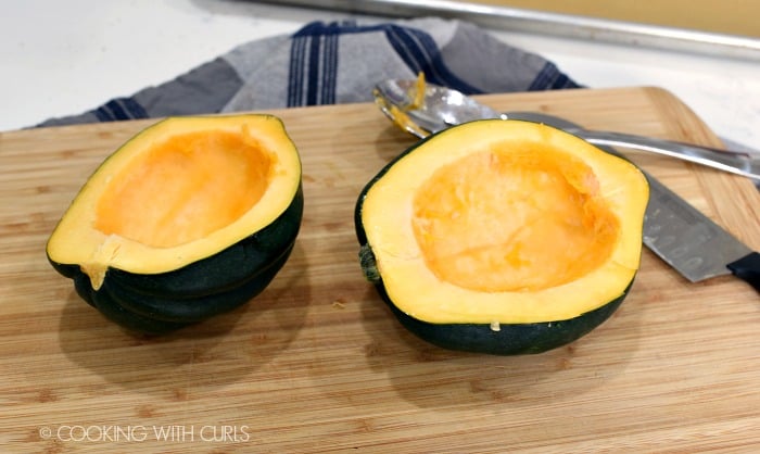 Two acorn squash halves with the seeds removed, sitting on a wood cutting board 