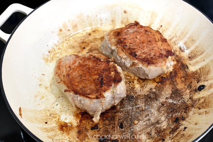 Two pork chops cooked on one side in a cast iron skillet 