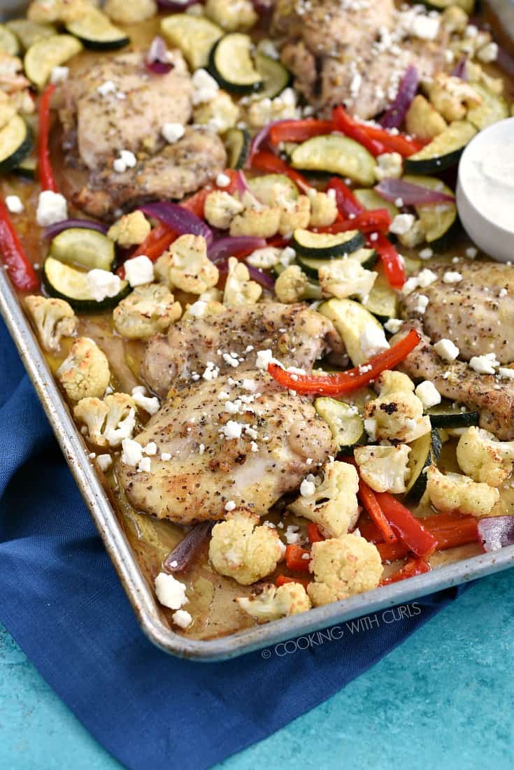 Chicken and vegetables on a parchment lined sheet pan topped with feta cheese