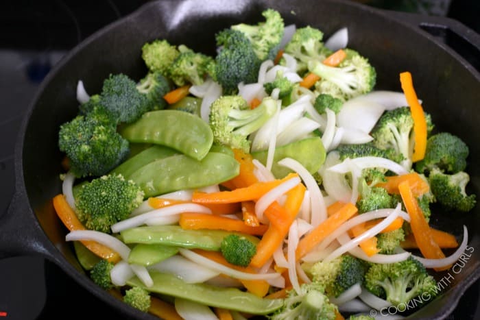 Broccoli, onion, snap peas and orange bell pepper slices in a cast iron skillet.
