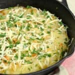 Duck Fat Pommes Anna in a cast iron skillet topped with grated cheese and parsley