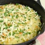 Sliced potatoes baked in a cast iron skillet topped with cheese and parsley