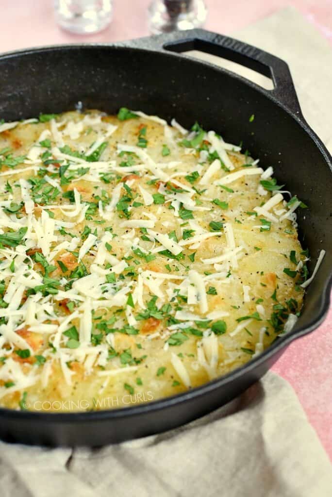 Sliced potatoes baked in a cast iron skillet topped with cheese and parsley