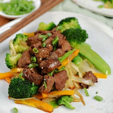 Korean BBQ Steak Tips served over stir-fry vegetables and garnished with sesame seeds and green onions.
