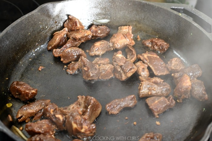 Marinated steak tips in a hot cast iron skillet.