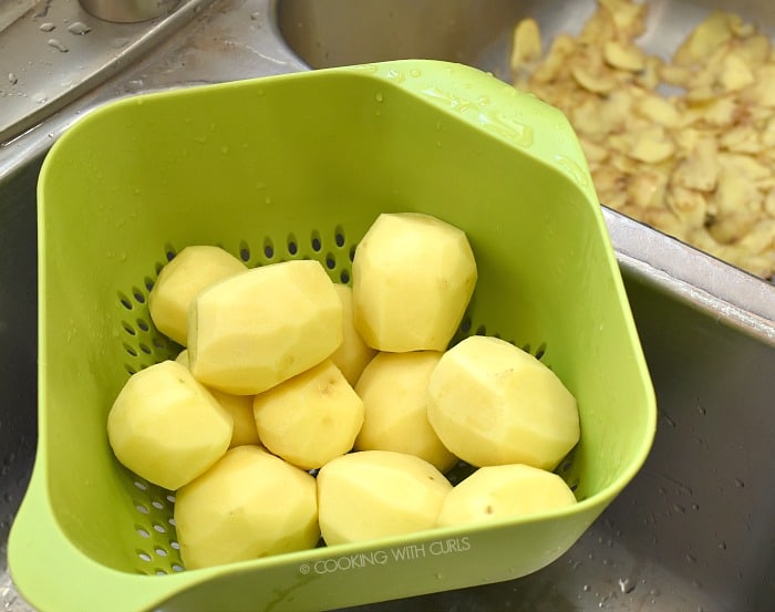 Peeled potatoes draining in a green colander 