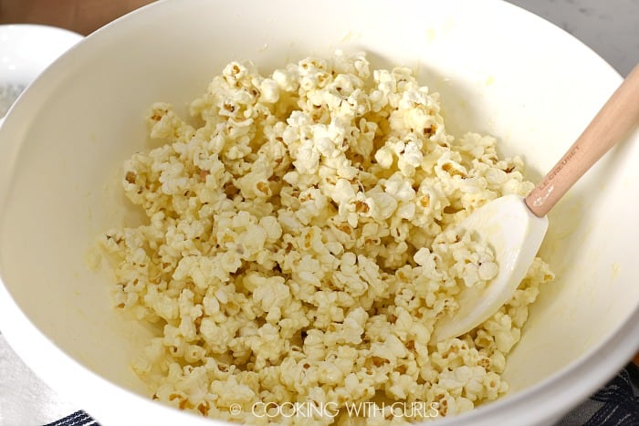 Popcorn mixed with the white chocolate in a large white bowl 