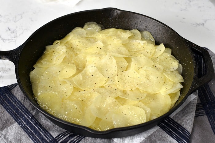 Several layers of sliced potatoes, duck fat, salt and pepper in a cast iron skillet