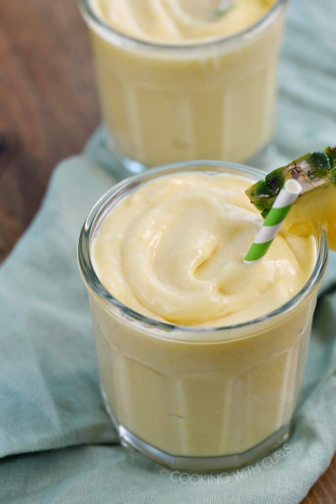 Two glasses filled with Mango Pina Colada Smoothie garnished with a pineapple wedge and green and white striped straw