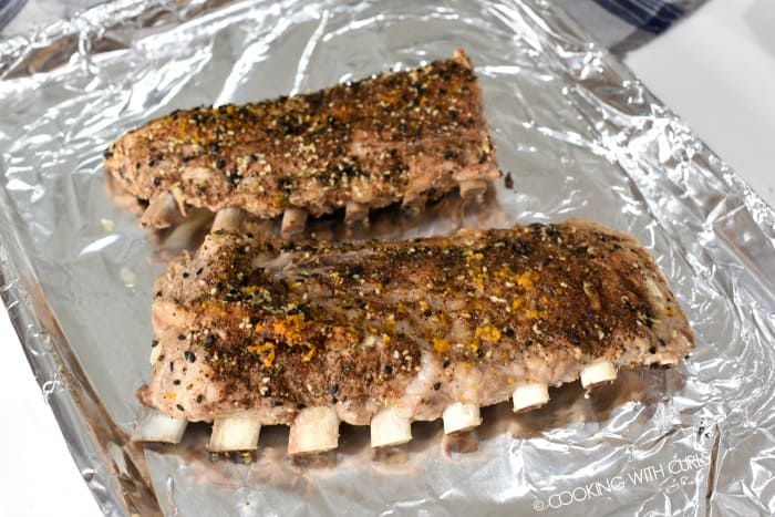 Two racks of ribs on a foil lined baking sheet 